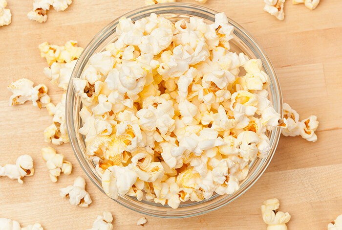 A bowl of plain popcorn on a wooden surface.